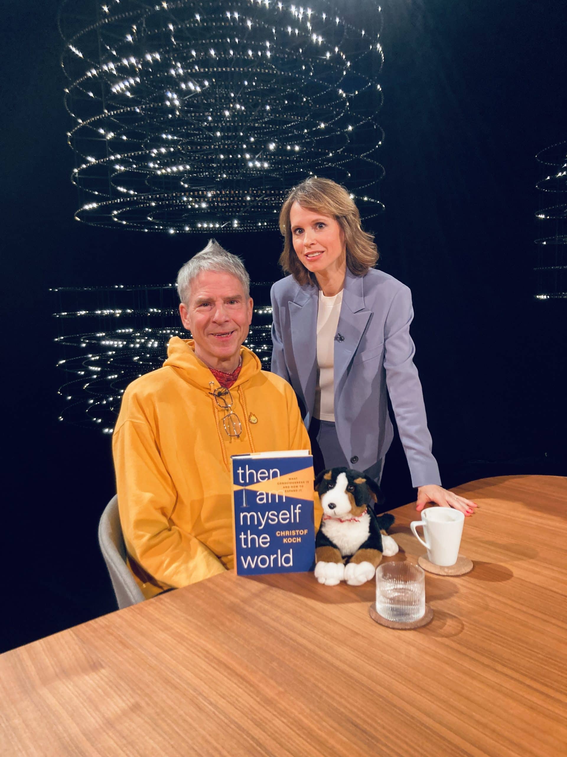 Barbara Bleisch im Gespräch mit Gast, sitzend an einem Tisch mit Buch und Plüschtier.